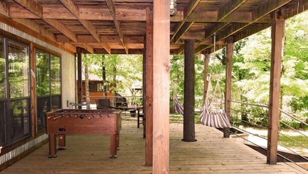 A wooden deck with a foosball table, a hammock, and a view of a forested area.