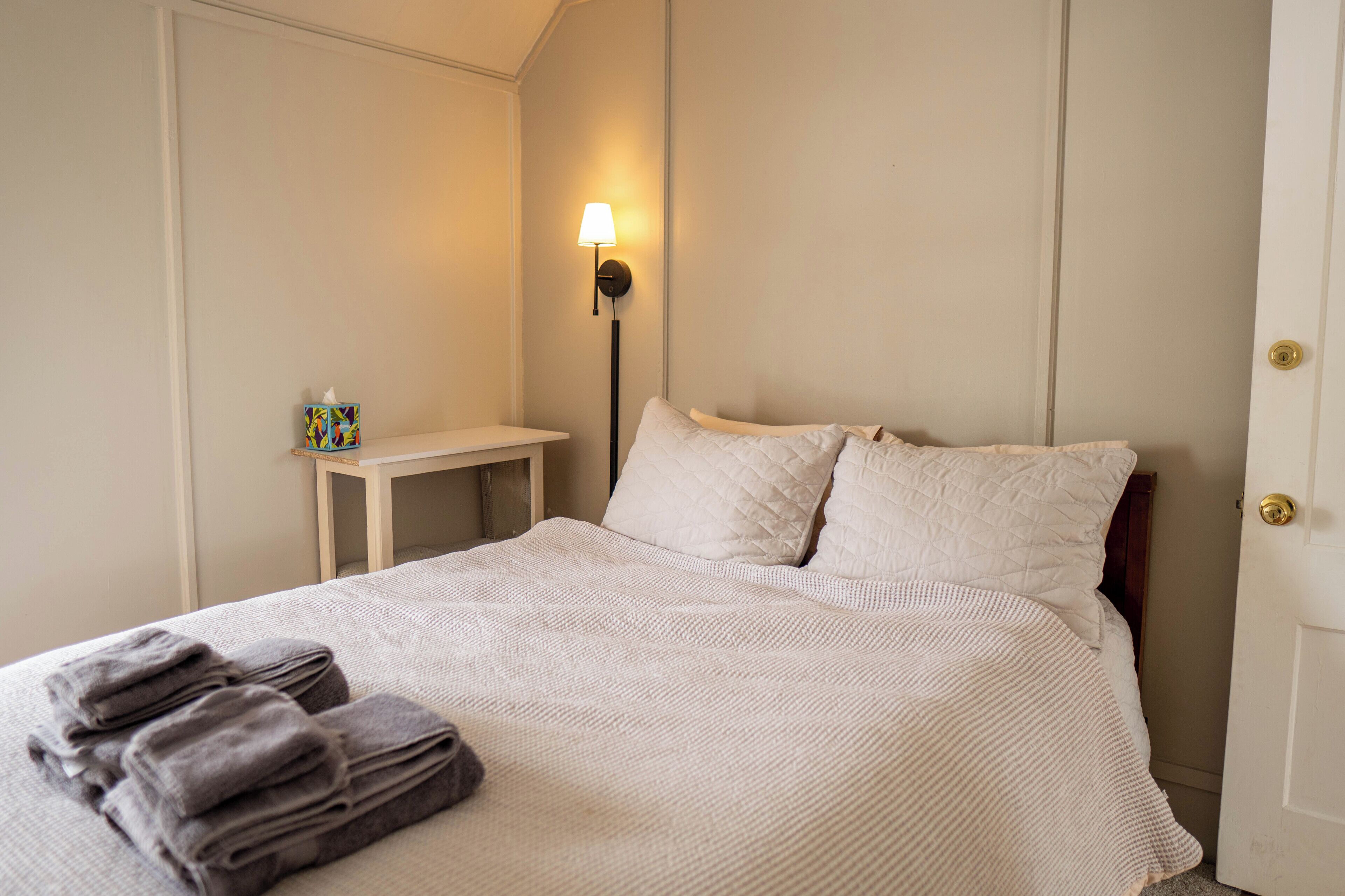 A neatly made bed with a white quilt, a bedside table with a lamp, and a small box of tissues.
