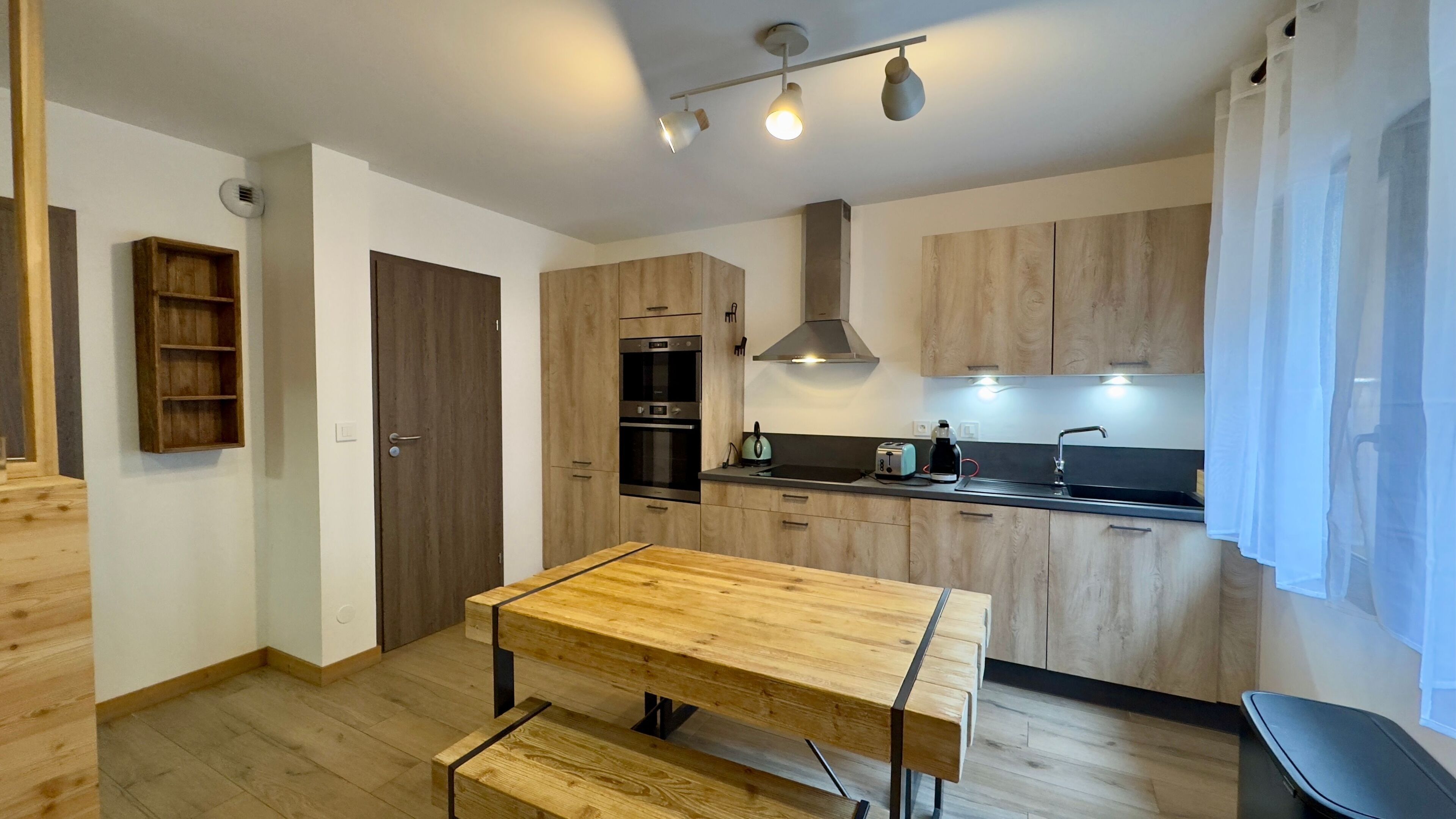 A modern kitchen with wooden cabinets, a built-in oven, a gas stove, and a dining table with benches.