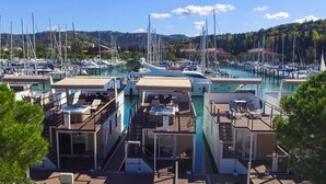 Ein Yachthafen mit mehreren vertäuten Booten, ein modernes Gebäude mit Außenbestuhlung und freiem Blick auf die umliegenden Hügel.