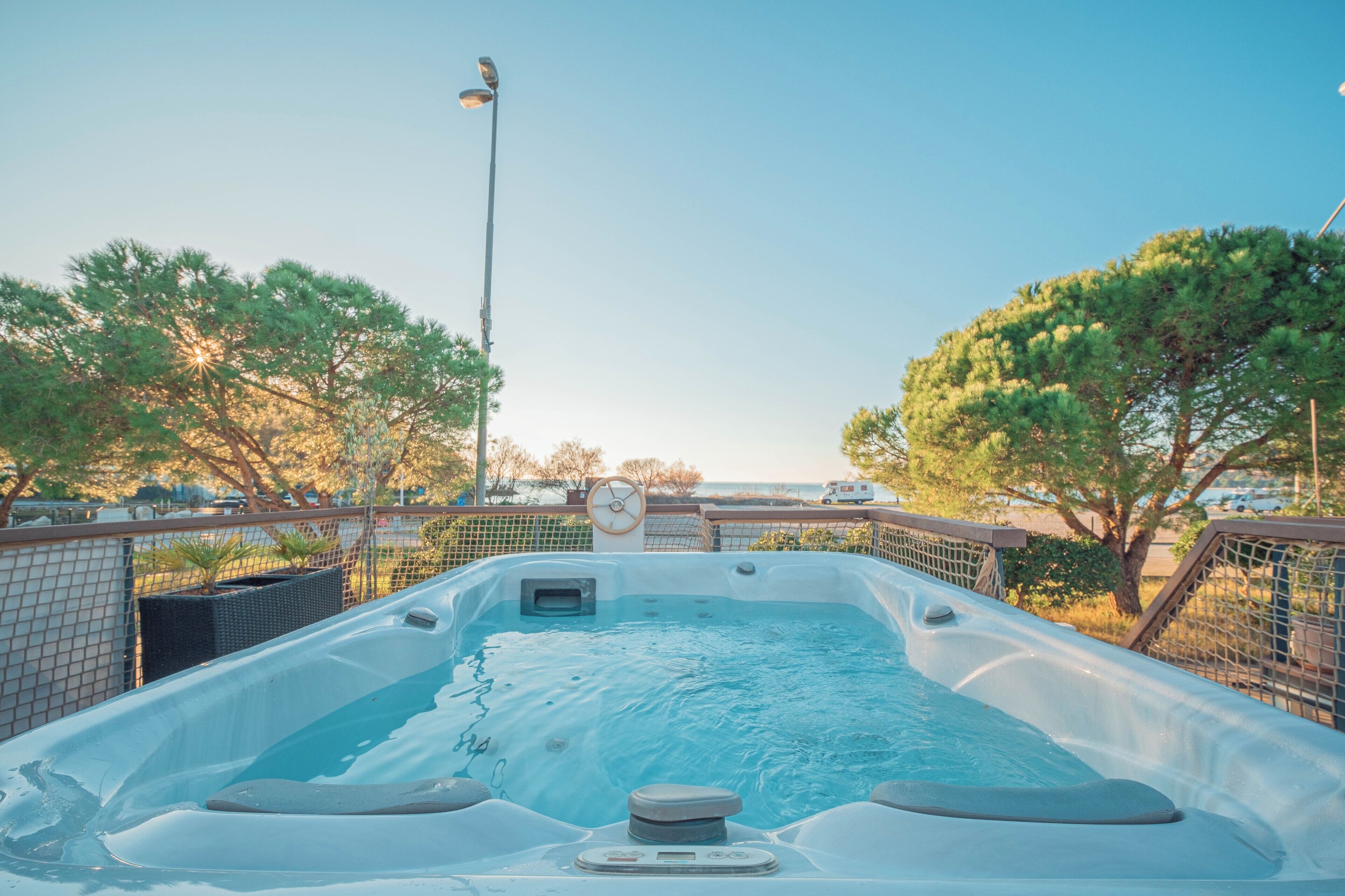 Un jacuzzi con panel de control, rodeado por una cerca, árboles y una farola.