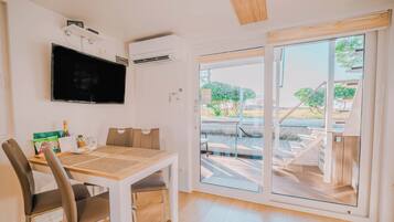 A modern room with a flat-screen TV, a dining table with chairs, a sliding glass door to an outdoor area, and an air conditioning unit.