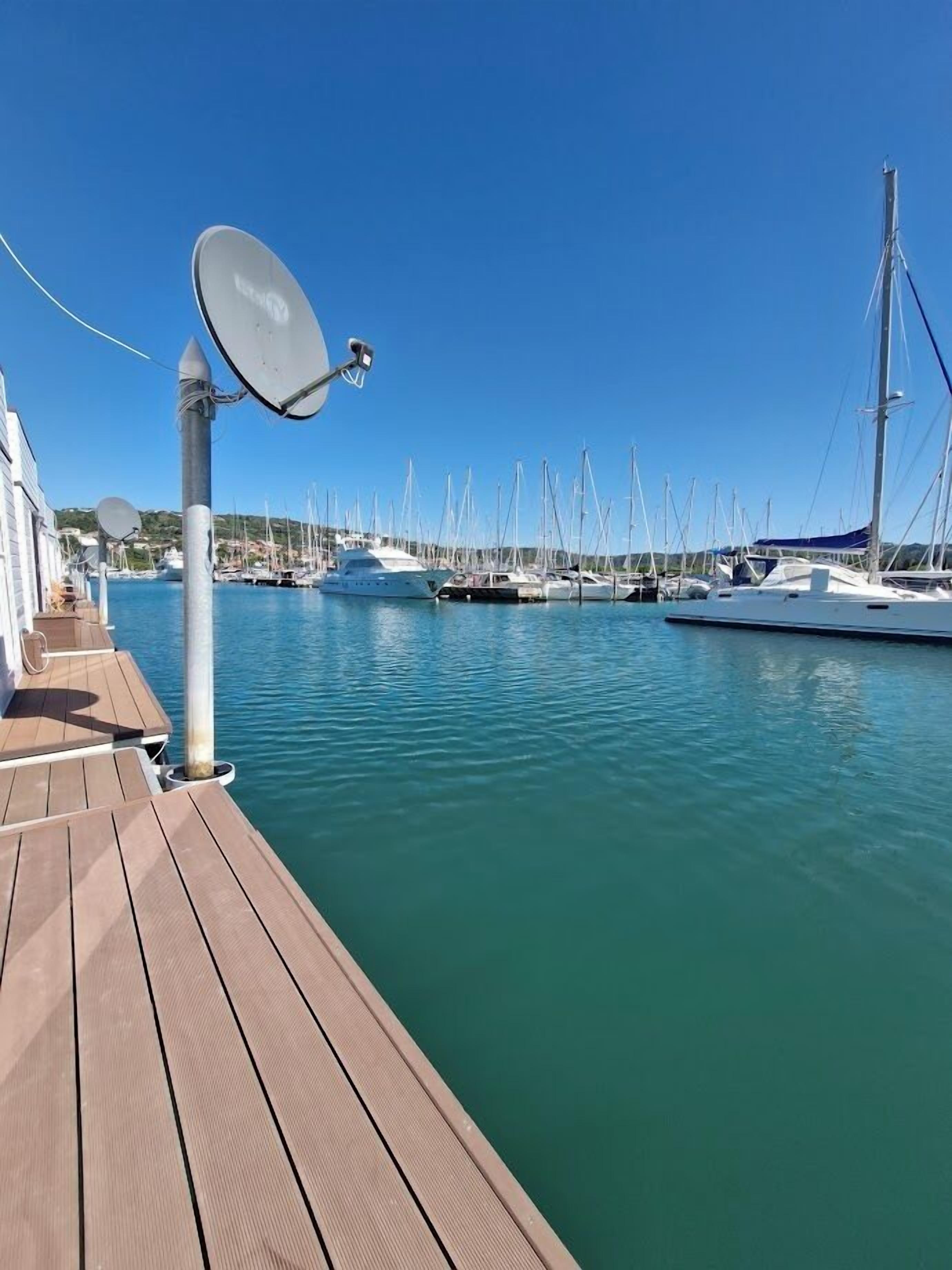 A marina with multiple yachts docked, a wooden deck, and a satellite dish.