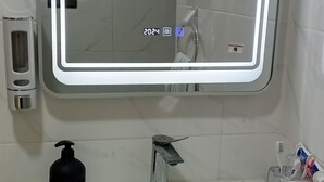 A bathroom with a white sink, a mirror with a light, a soap dispenser, and a toothbrush holder. - Nice house in the middle of Oujda city (Oujda)