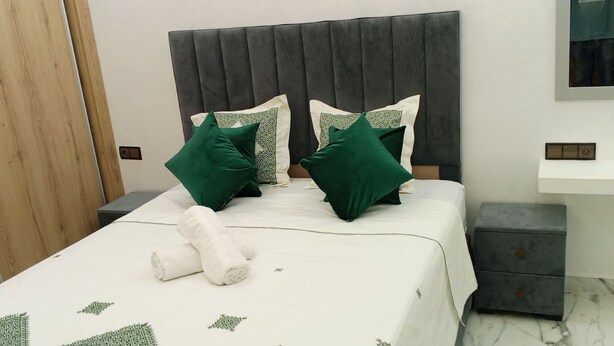 A neatly made bed with green and white pillows, a white towel, and a marble floor. - Nice house in the middle of Oujda city (Oujda)