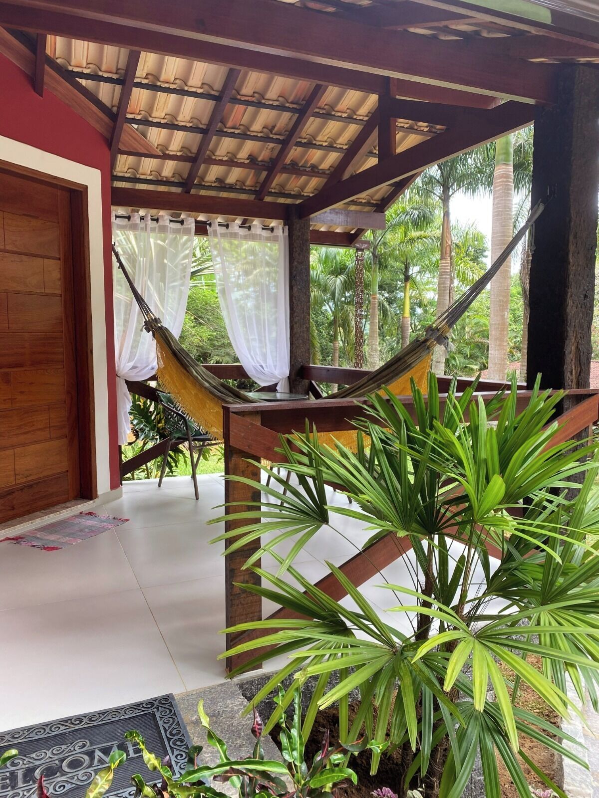 A hammock under a wooden pergola, a door, and a welcome mat.