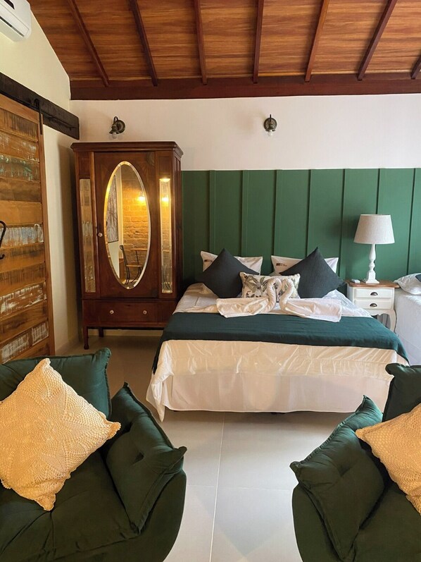 A bedroom with a bed, two green armchairs, a wooden wardrobe, and a nightstand with a lamp. - Pousada Brisa Do Vale (Barra do Piraí)