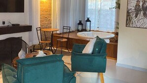 A living room with a fireplace, teal armchairs, a dining area with a table and chairs, a TV mounted on the wall, and a large window with curtains. - Pousada Brisa Do Vale (Barra do Piraí)