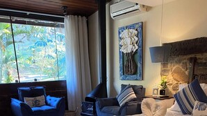 A bedroom with a bed, a blue armchair, a sofa, a small wooden stool, and a stone wall. - Pousada Brisa Do Vale (Barra do Piraí)