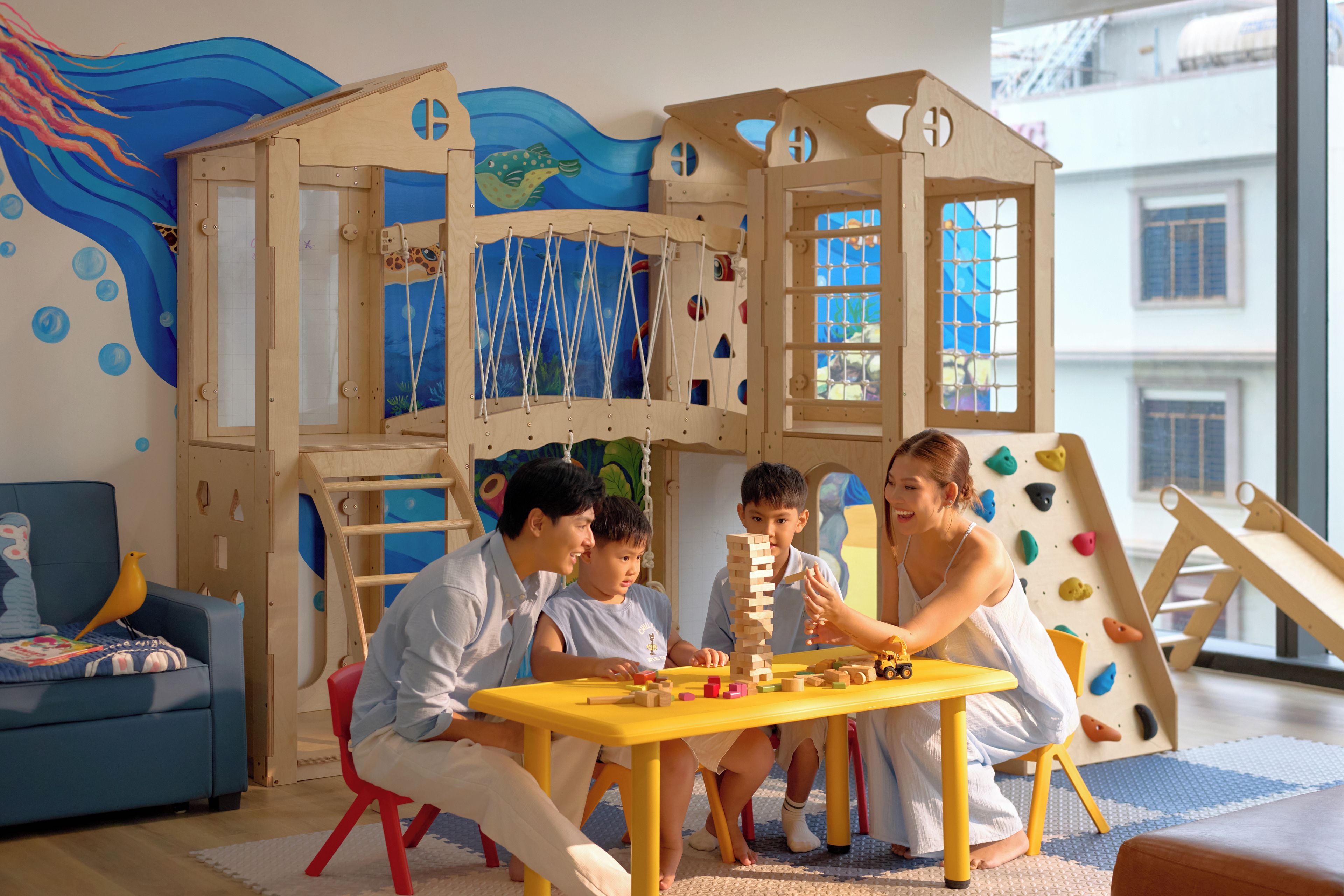 Área de recreação infantil com um parquinho de madeira, uma mesa com blocos de madeira e um sofá azul.