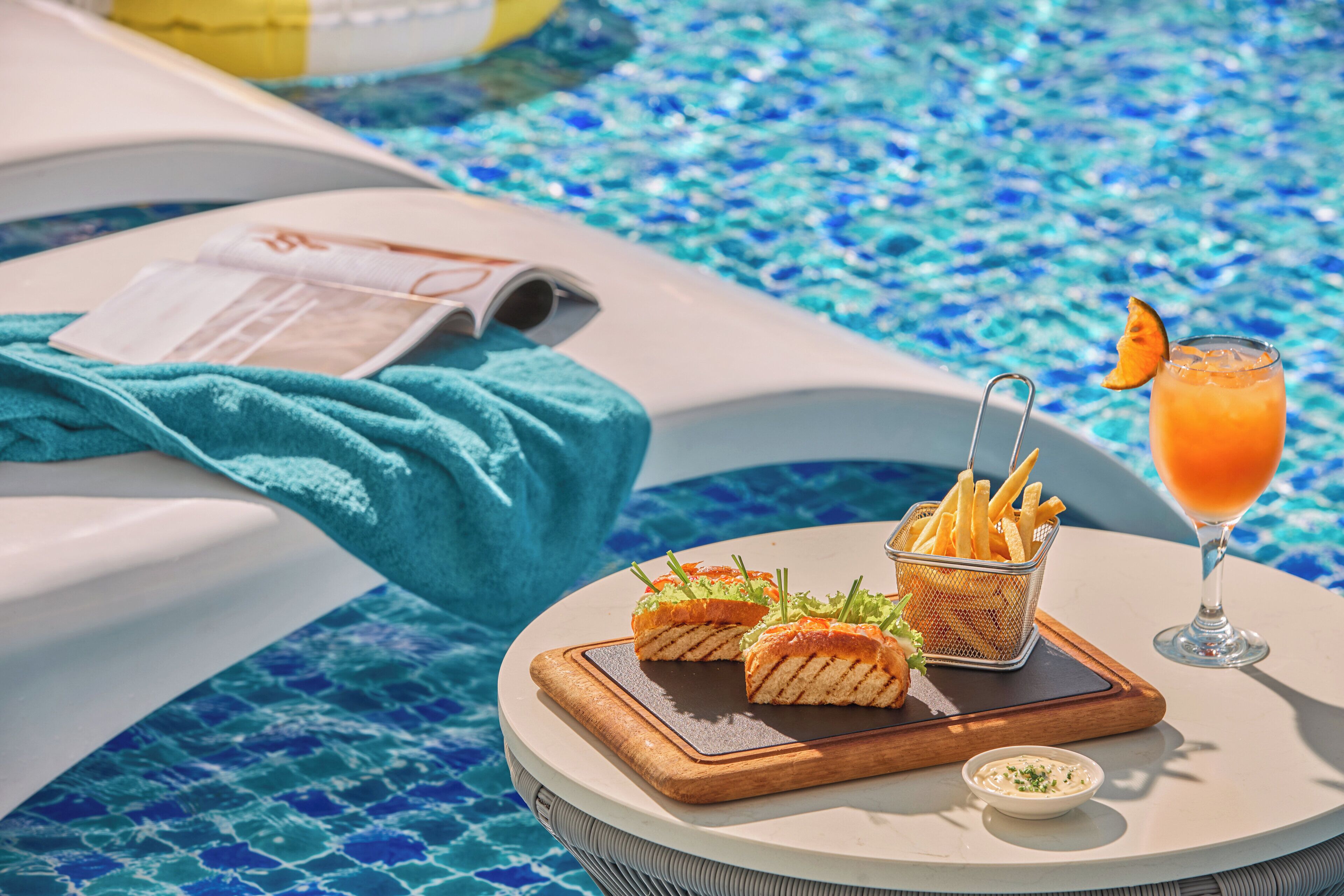 A poolside dining setup with a menu, a basket of fries, a drink, and a small bowl of sauce.