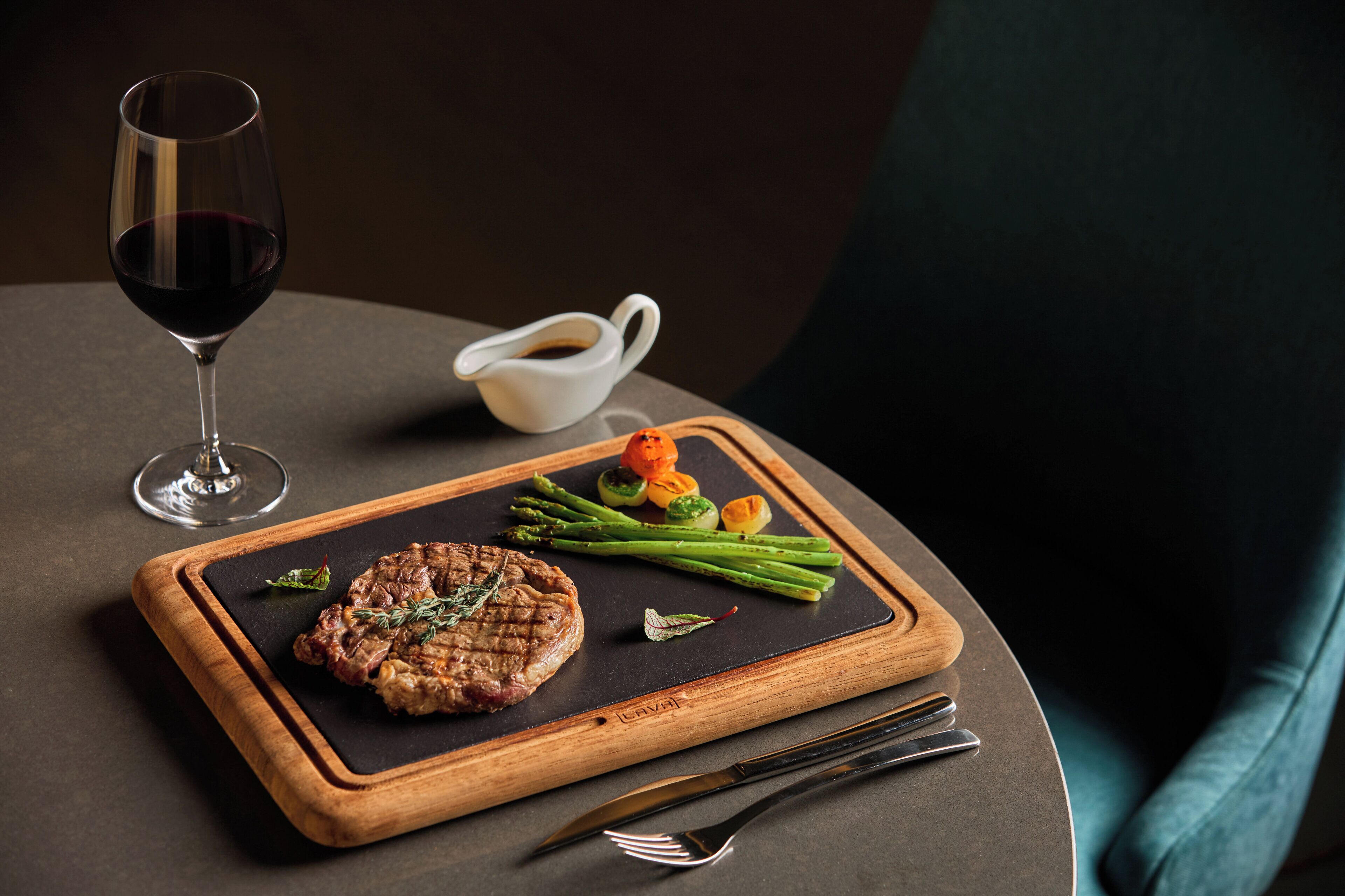 Une table à manger avec un steak, des asperges et un verre de vin rouge.
