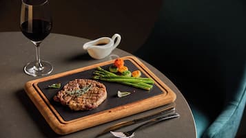 Une table à manger avec un steak, des asperges et un verre de vin rouge.