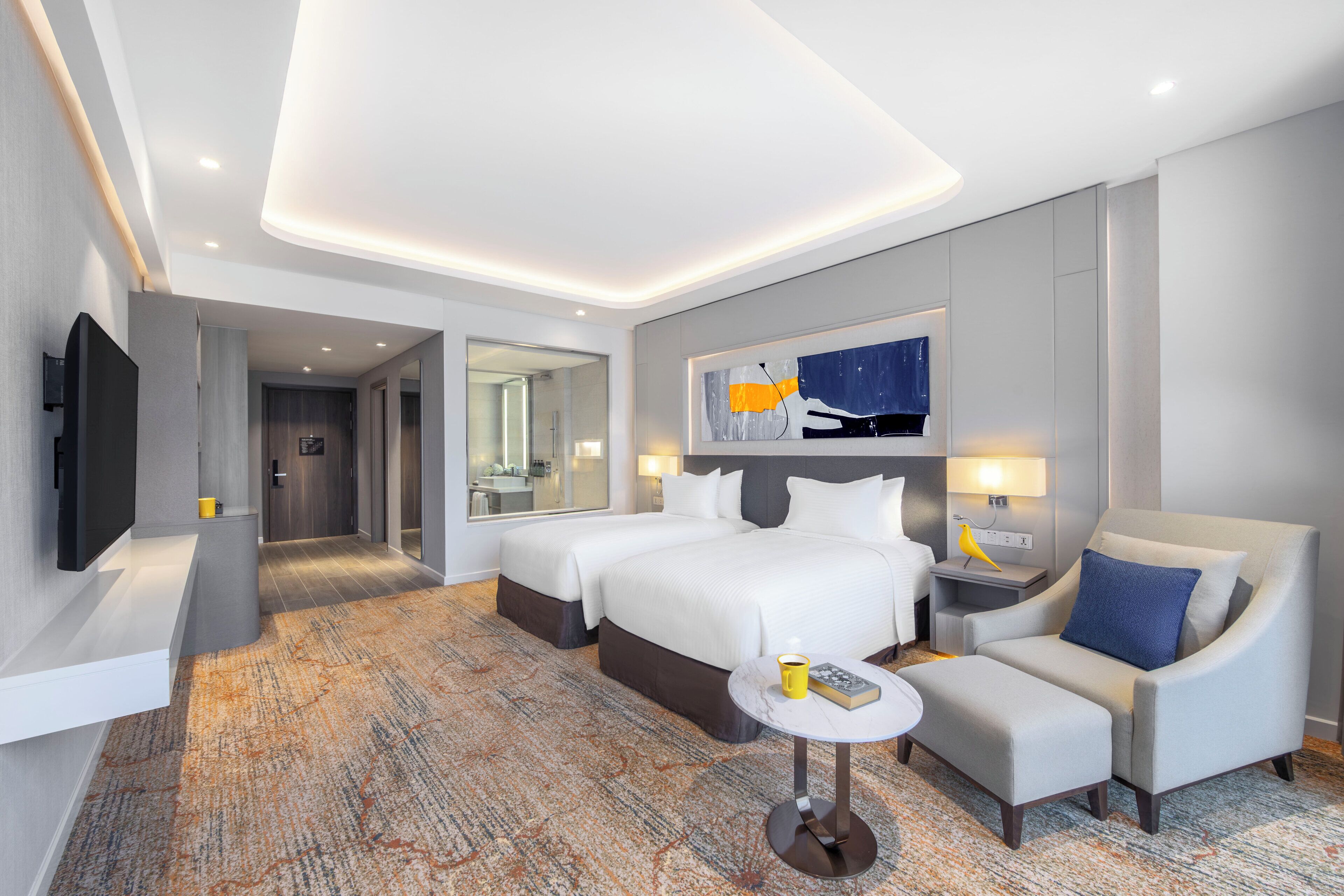 A modern hotel room with a large bed, two bedside tables, a flat-screen TV, a sofa, and a small round table.