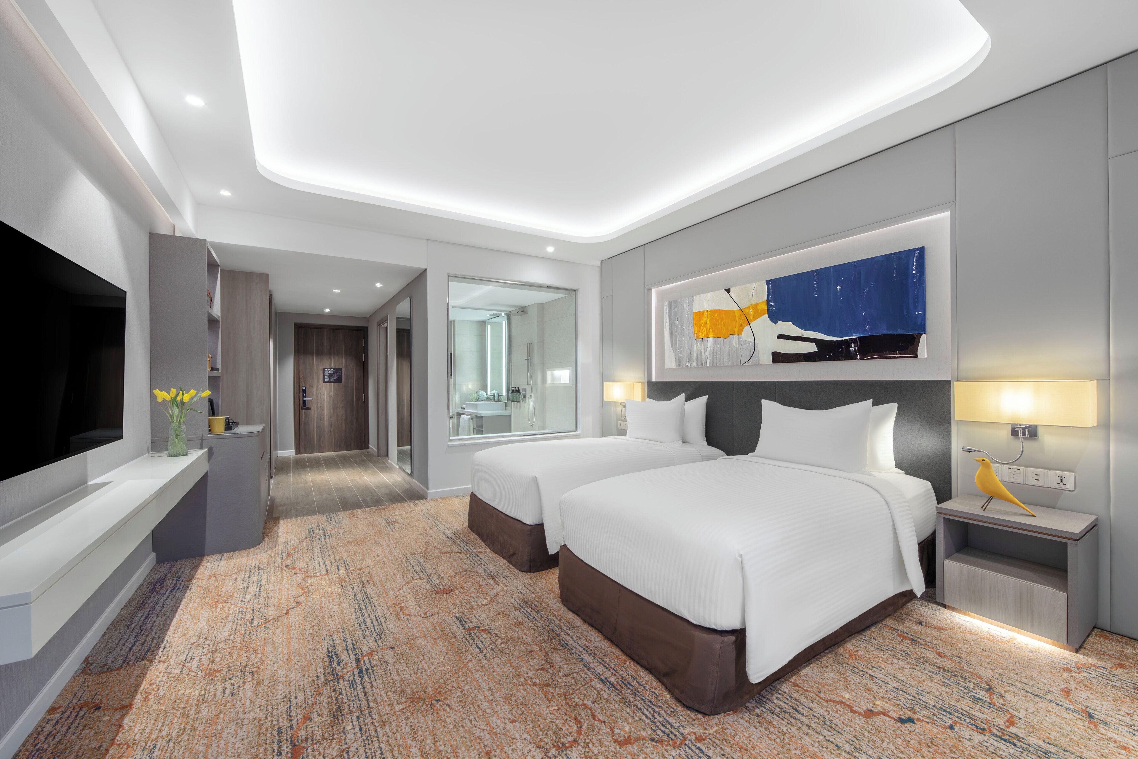 A hotel room with two beds, a flat-screen TV, a painting, and a nightstand with a lamp and a bird figurine.