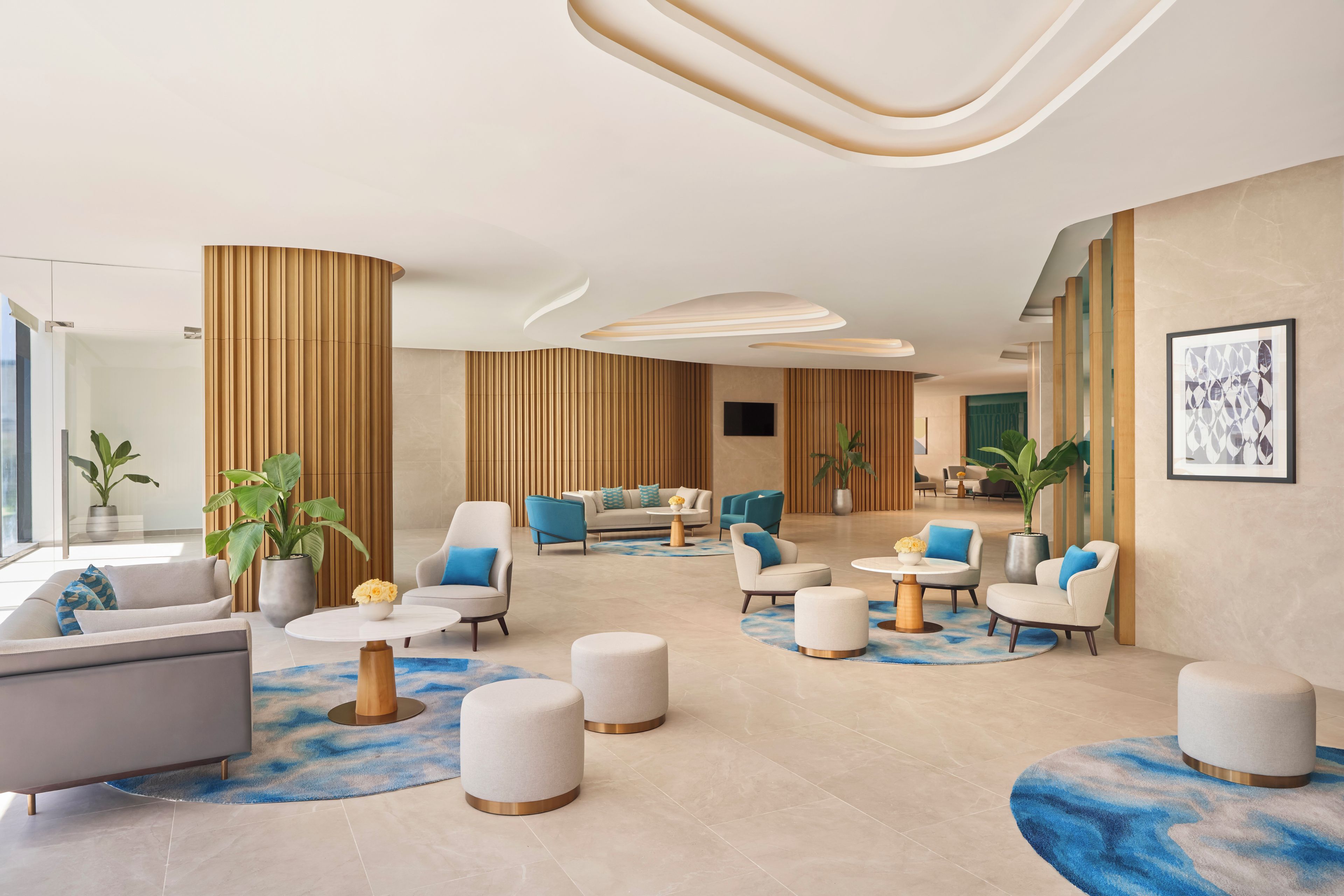 A modern lobby with a central seating area, sofas, armchairs, and ottomans arranged around a coffee table.