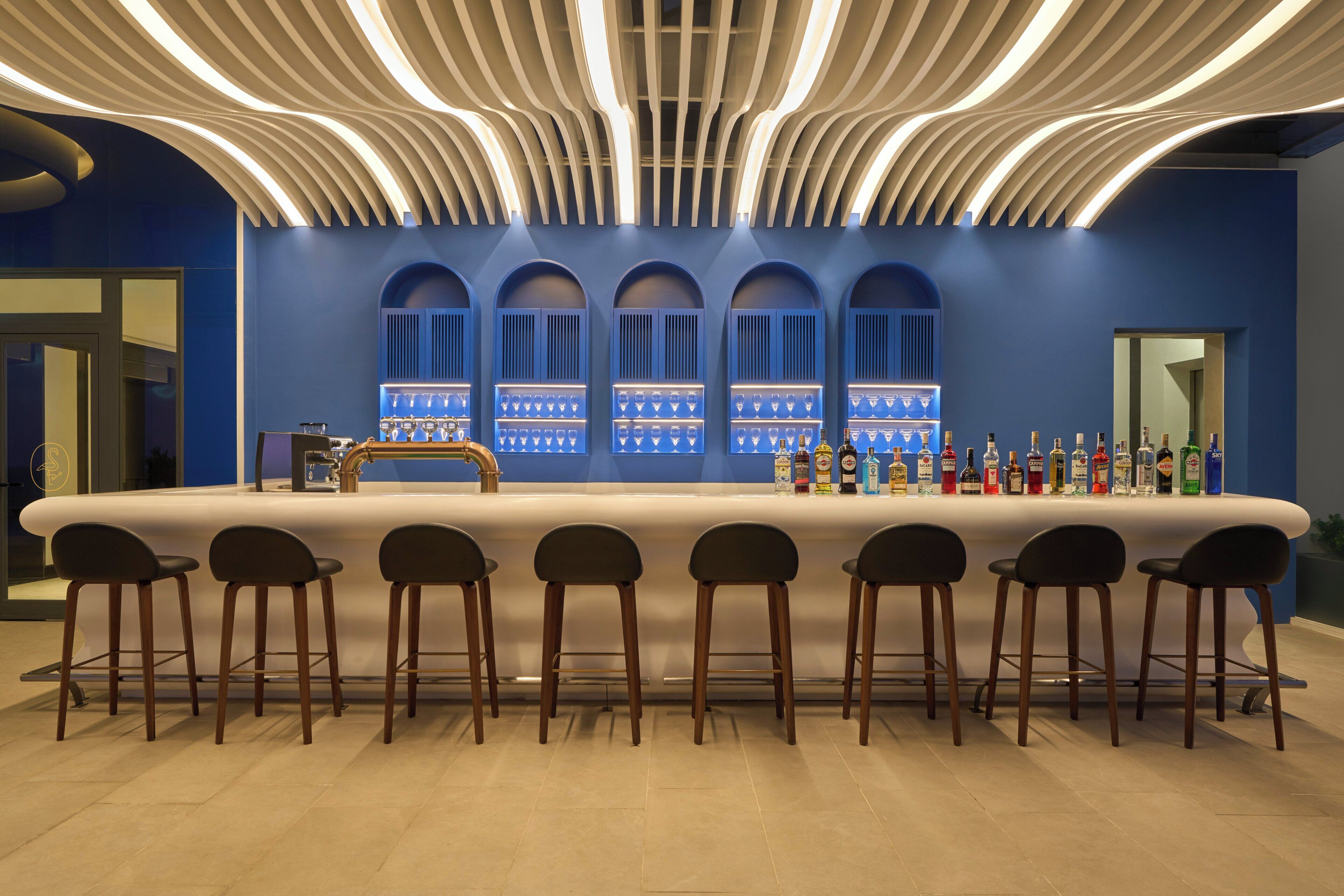 A bar area with a long counter, multiple stools, and a selection of bottles.