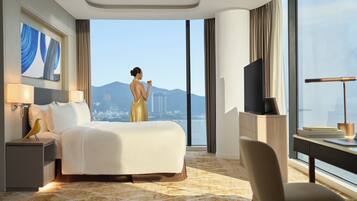 A hotel room with a large bed, a desk, a chair, a TV, and a view of a cityscape.