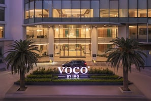 A modern building with a prominent entrance, palm trees, and a sign reading 'VOCO BY IHG'. - voco Scenia Bay Nha Trang by IHG (Bac Nha Trang)