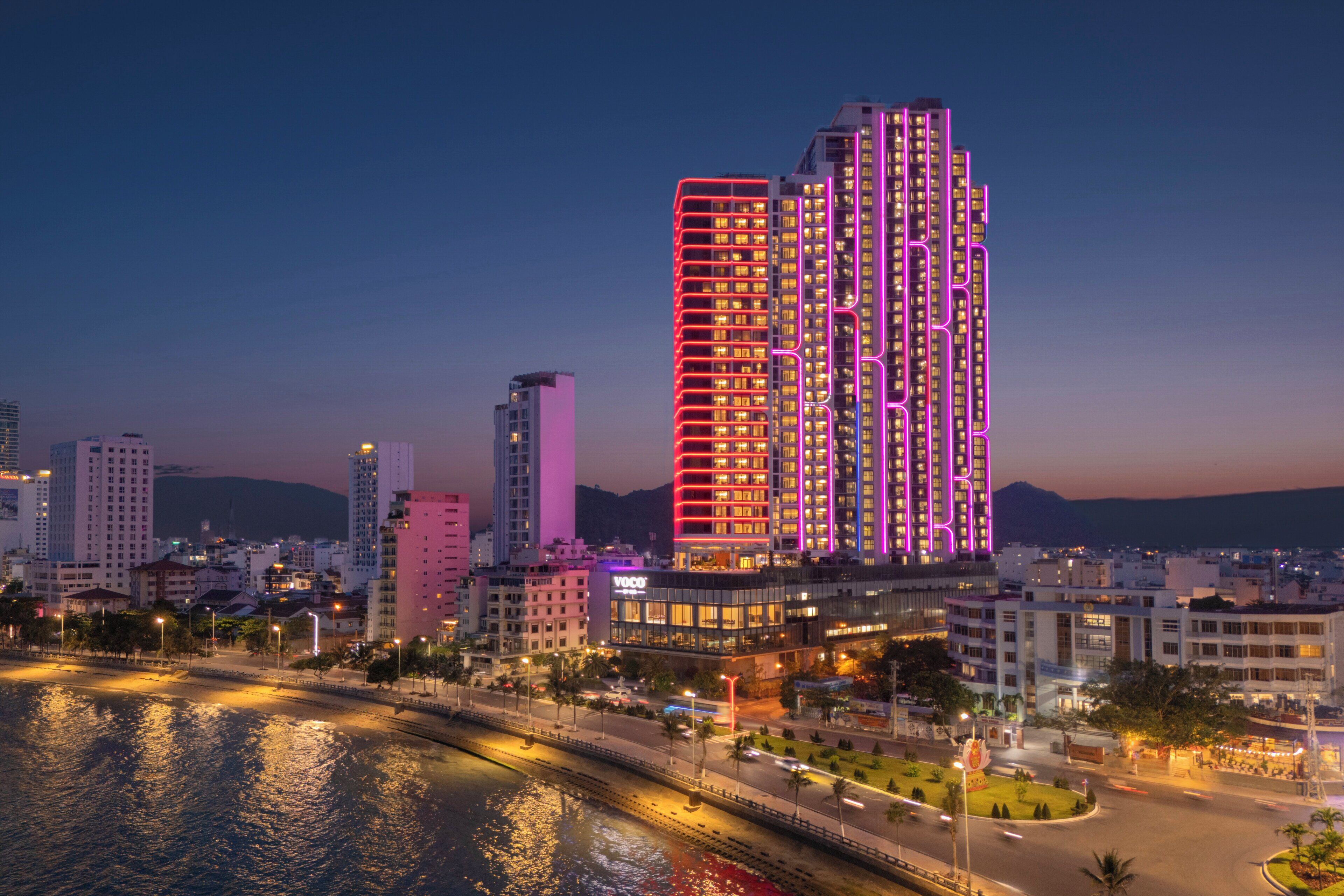 A high-rise building with multiple floors, surrounded by other buildings and a body of water.