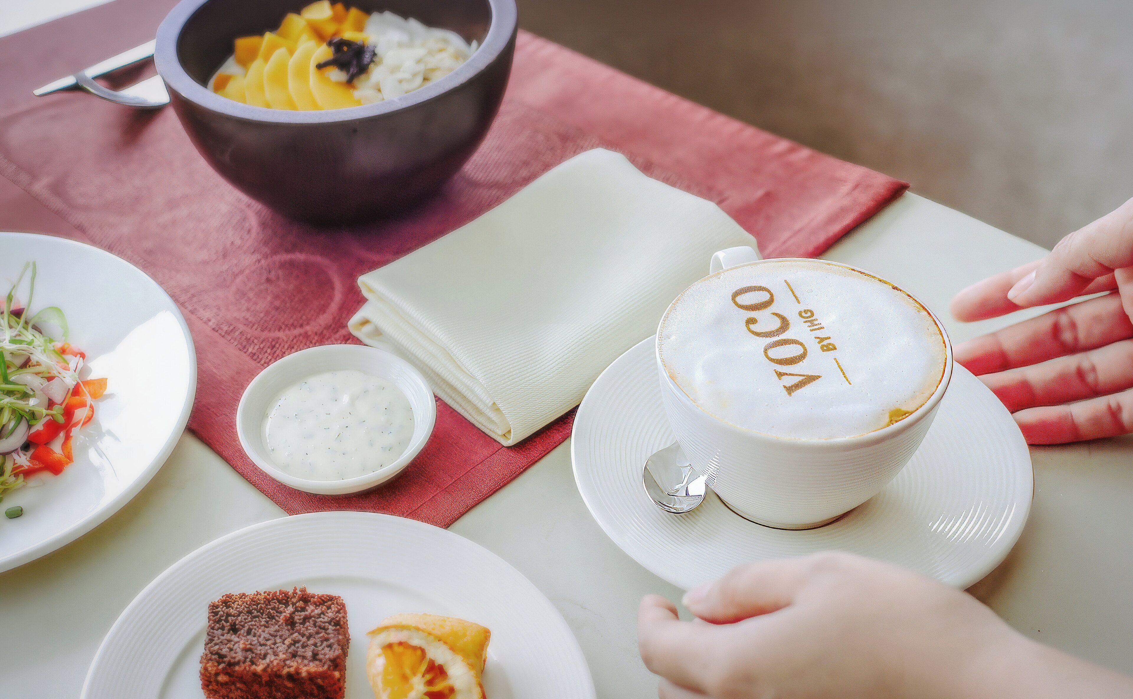 A table with a cup of coffee, a bowl of soup, a plate of food, and a napkin.