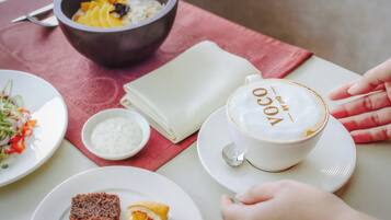 A table with a cup of coffee, a bowl of soup, a plate of food, and a napkin.