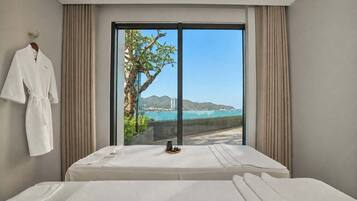 A hotel room with a bed, a robe hanging on the wall, and a view of the sea and mountains.