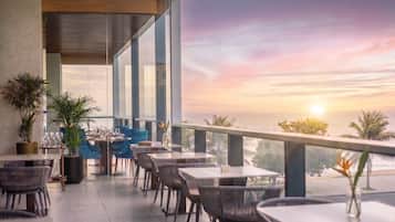 Un espace extérieur aménagé pour les repas, avec des tables et des chaises, offrant une vue panoramique sur un magnifique coucher de soleil.