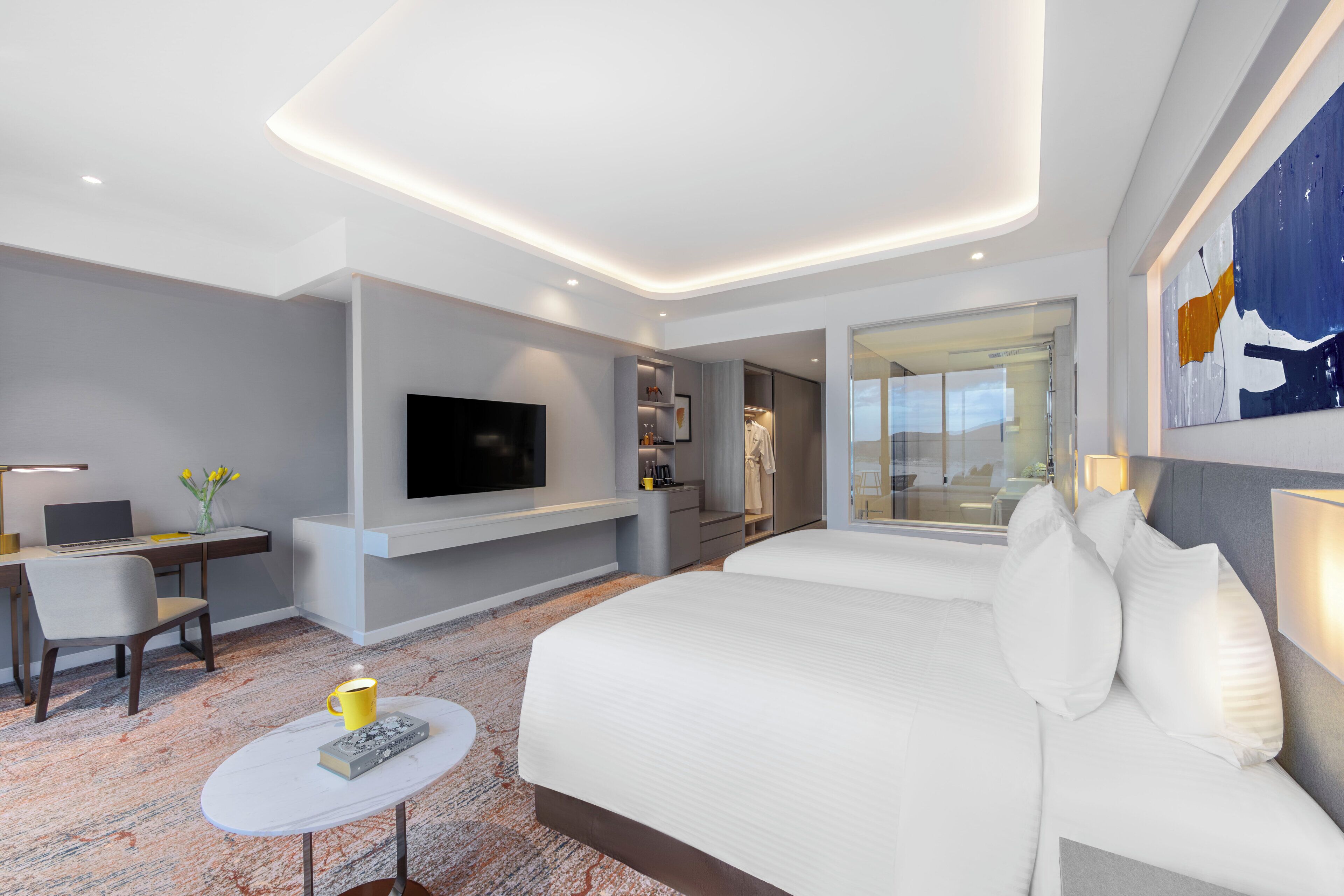 A modern hotel room with a large bed, a flat-screen TV, a desk with a laptop, and a seating area with a small table and chair.