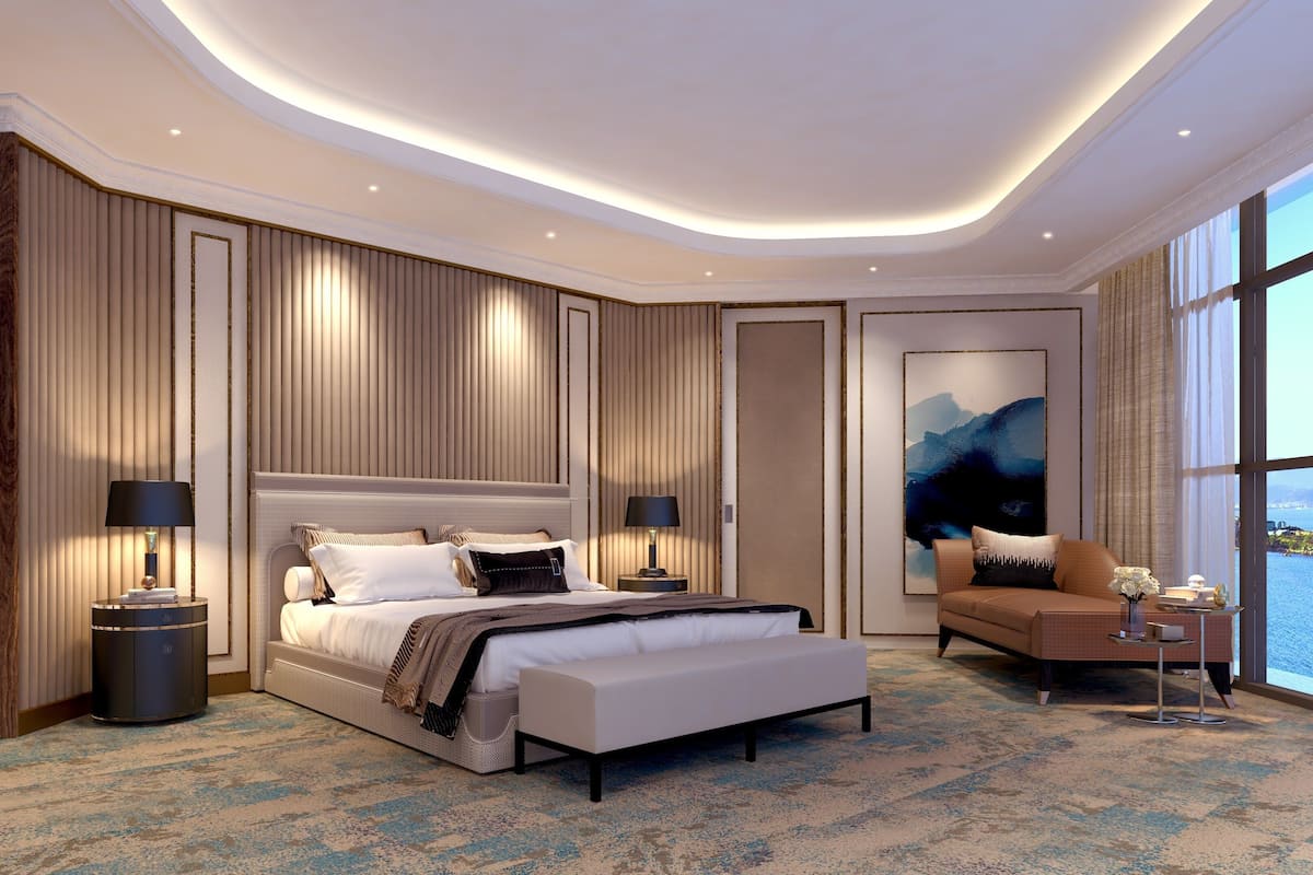 A modern bedroom with a large bed, bedside tables, a desk, and a view of the sea.