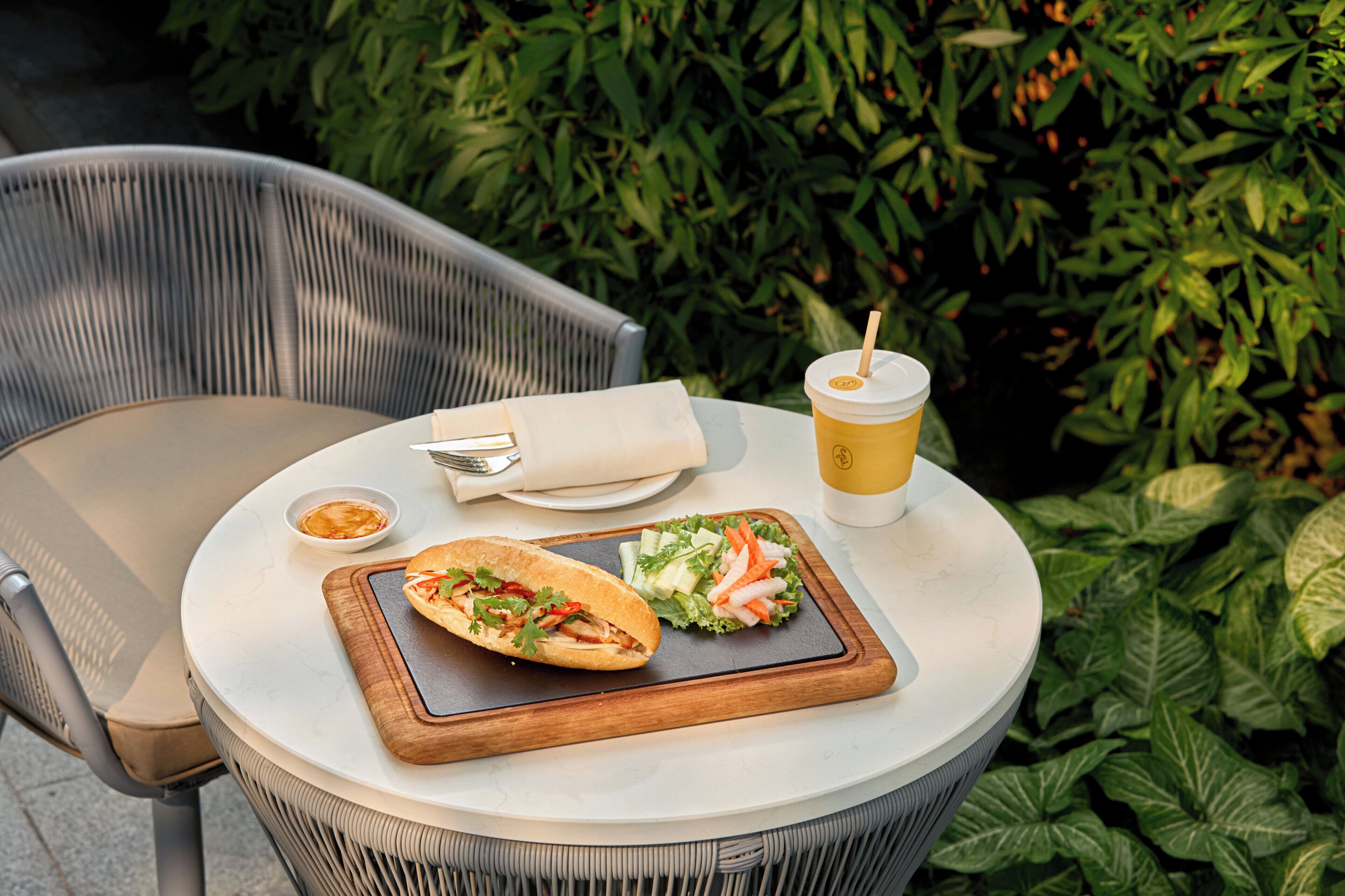 A round table with a sandwich, a cup, and a small bowl of sauce.