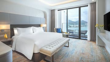 Ein modernes Hotelzimmer mit einem großen Bett, einer Bank, einem Schreibtisch und Blick auf die Stadt durch große Fenster.