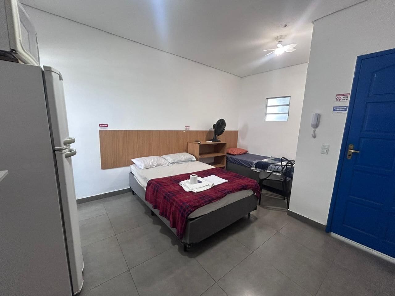 A small, clean room with a bed, a desk, and a blue door.