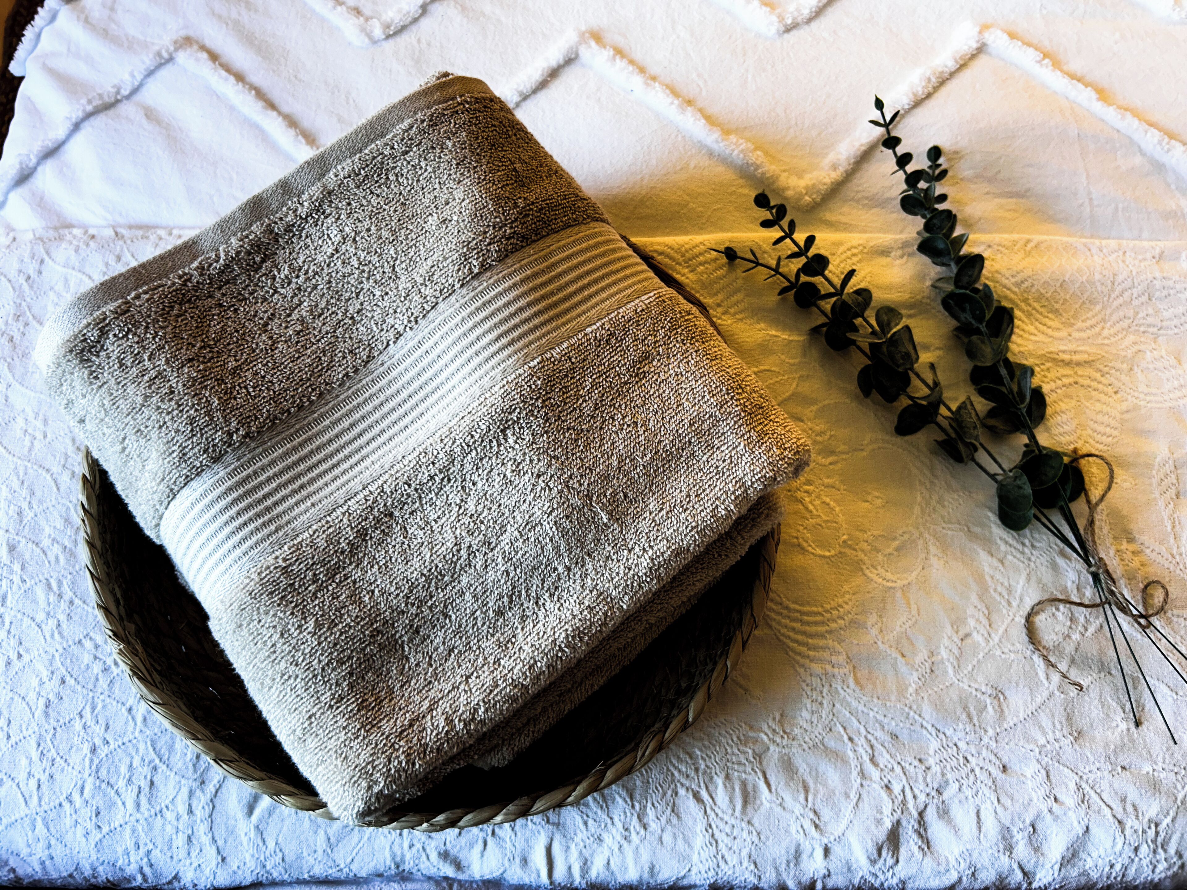 A neatly folded towel on a textured white bedspread with a decorative branch.