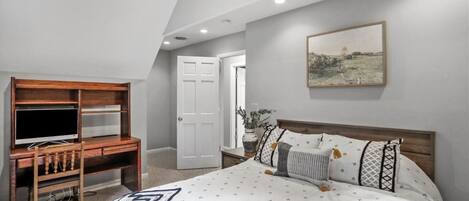 A bedroom with a bed, a desk, and a door leading to another room.
