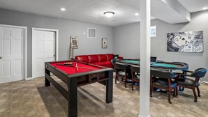 A room with a pool table, a red leather couch, a card table, and a pool table with chairs. - Deep Forest Dream- Aunt Susies Raystown Lake (James Creek)