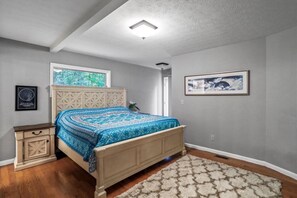 Un dormitorio con cama, mesita de noche, ventana y un cuadro en la pared.