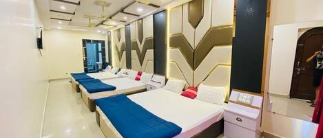 A hotel room with three beds, each with a blue blanket, white pillows, and a control panel on the side.