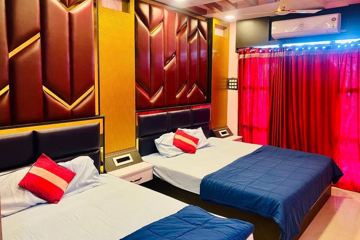 Une chambre d’hôtel avec deux lits, chacun recouvert d’une couvre-lit d’une couleur différente, une tête de lit ornée d’un motif géométrique et un rideau rouge à la fenêtre.