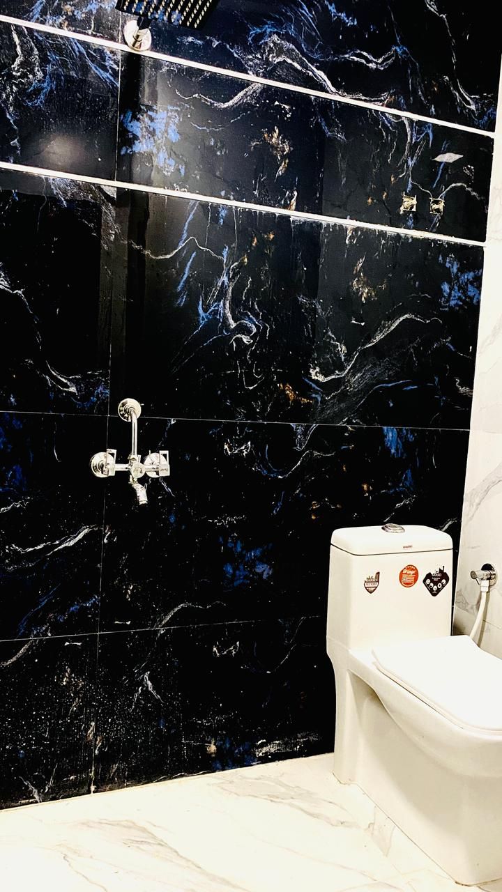 Ein Badezimmer mit schwarzen Marmorfliesen, einer weißen Toilette und einer Dusche mit Chromarmaturen.