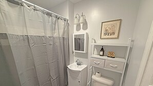 A bathroom with a shower curtain, sink, mirror, toilet, and a framed picture on the wall.