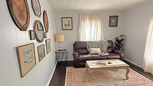 A living room with a brown leather sofa, a coffee table, a rug, and framed pictures on the wall.