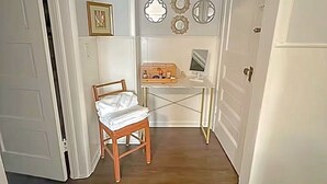 A narrow hallway with a wooden chair, a desk with a computer, and decorative wall mirrors.