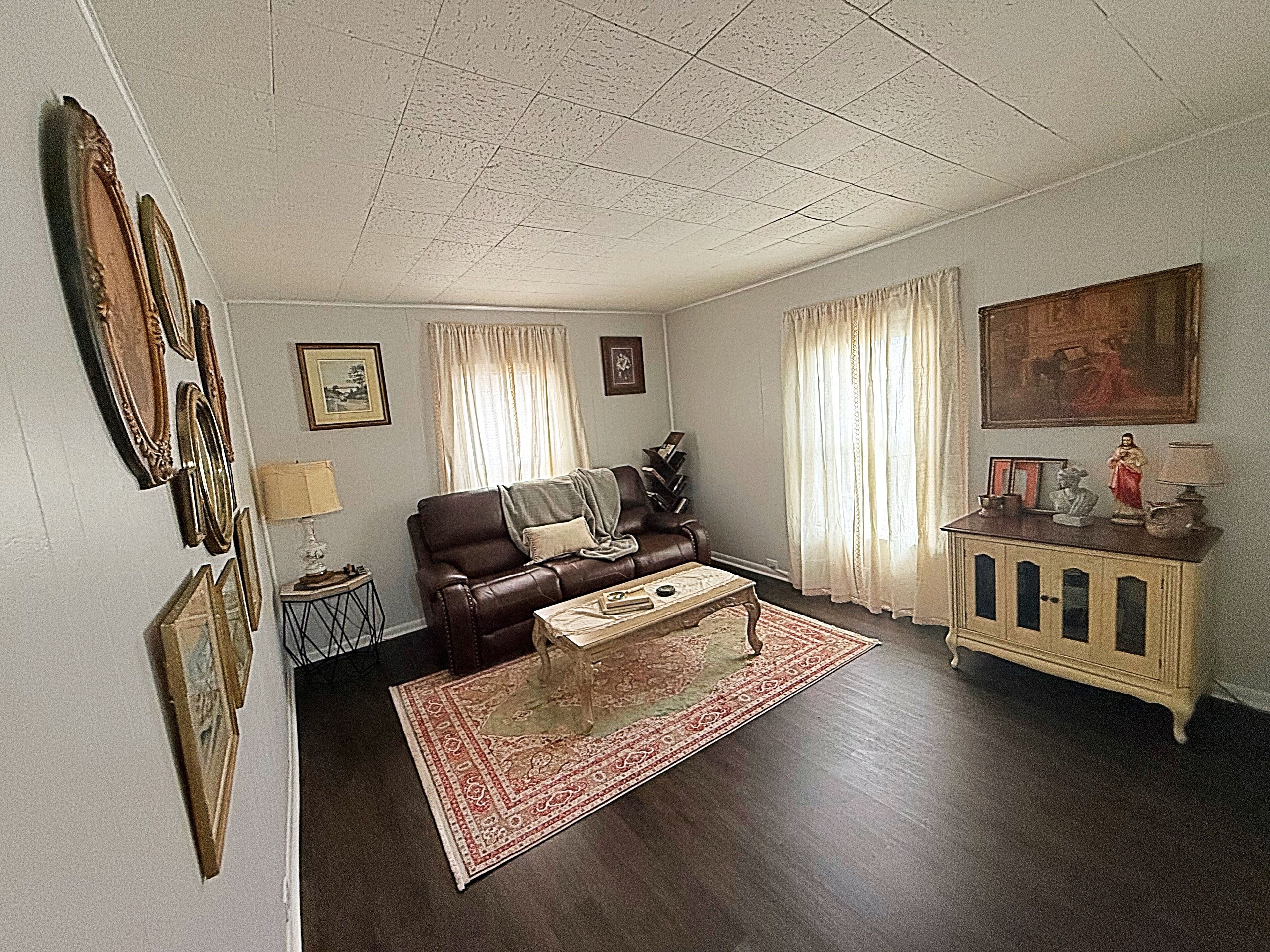 A living room with a brown leather sofa, a coffee table, a patterned rug, a cabinet with decorative items, and framed pictures on the walls.