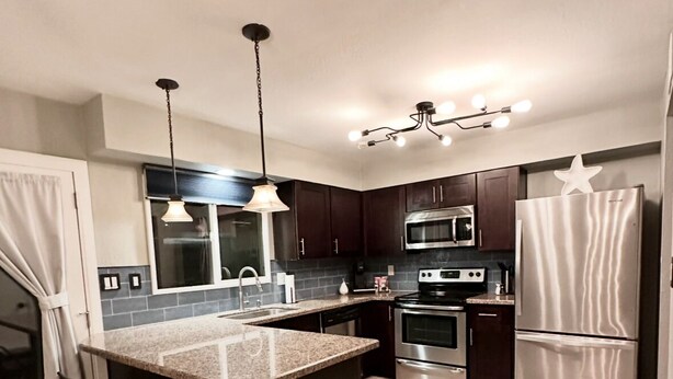 A modern kitchen with dark wood cabinets, a granite countertop, stainless steel appliances, and pendant lighting. - Rare 4 Bedroom Townhome with Backyard in Tempe (Tempe)