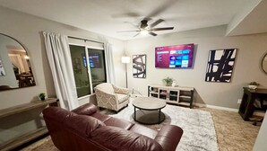 A living room with a brown leather couch, a round coffee table, a TV mounted on the wall, and a ceiling fan. - Rare 4 Bedroom Townhome with Backyard in Tempe (Tempe)