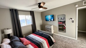 A hotel room with a bed, a ceiling fan, a TV, a mirror, and a window with curtains. - Rare 4 Bedroom Townhome with Backyard in Tempe (Tempe)