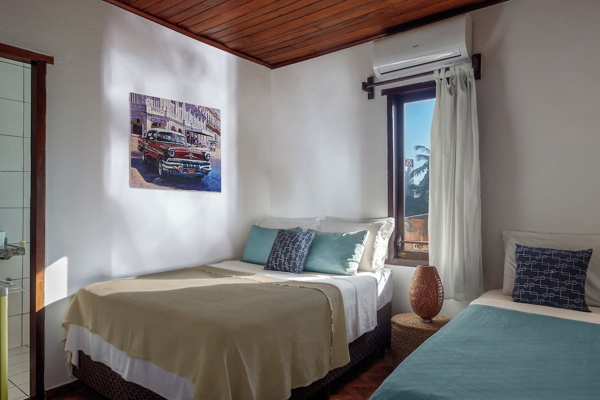 Un dormitorio con dos camas, un cuadro en la pared, una ventana con cortinas y vistas al exterior.