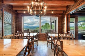 A wooden interior with a large dining table, chairs, and a view through large windows.