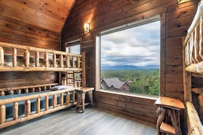A wooden cabin interior with a bench, a window with a view of a forest and mountains, and a wooden railing. - Indoor Golf Cabin w/ Amazing Views! Sleeps 40! (Sevierville)